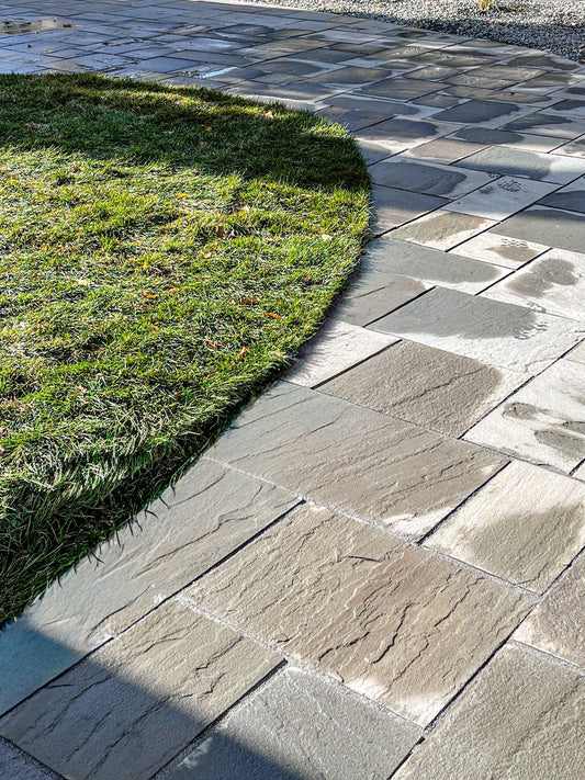 Natural bluestone patio installation in Minneapolis backyard featuring ashlar pattern layout and integrated garden wall.